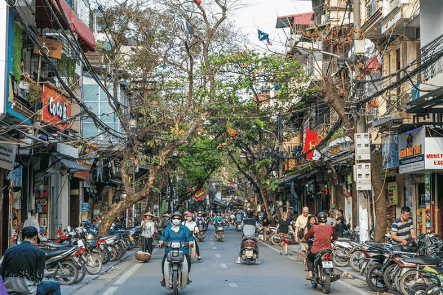 A crowded, lively street scene in Hanoi with motorbikes and local shops.