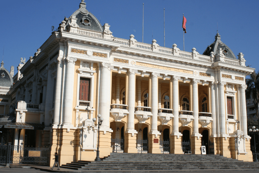 The Hanoi Opera House, a landmark 20th-century yellow building with neo-classical architecture and a grand stone staircase.
