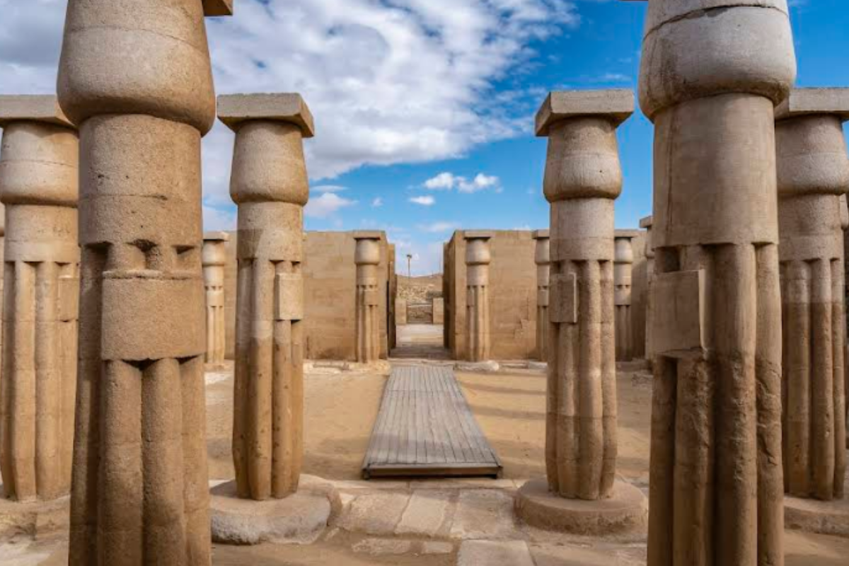 A ground-level, symmetrical shot of an ancient stone temple courtyard under a bright, partly cloudy blue sky.