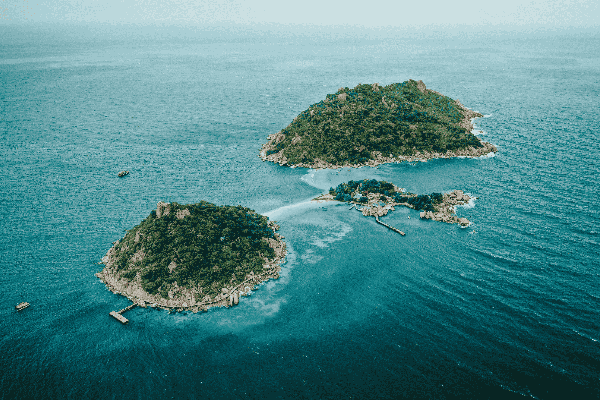 Aerial view of Ko Nang Yuan in Thailand, featuring three small, lush green islands connected by a white sandbar in the middle of a turquoise ocean.