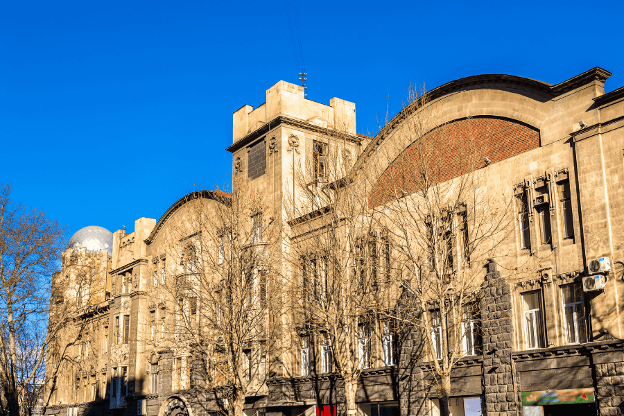 The facade of the historic Tbilisi Opera and Ballet Theater on Rustaveli Avenue, featuring distinctive neo-Moorish architecture with light and dark horizontal stripes and pointed arches.