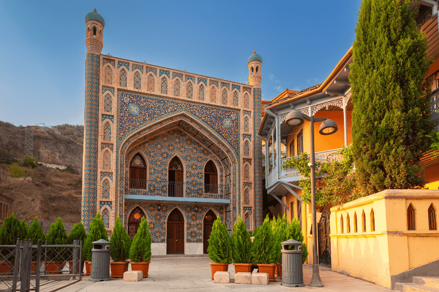 Orbeliani Sulfur Baths in Old Tbilisi with blue tiled mosaic archway and wooden balconies nearby.