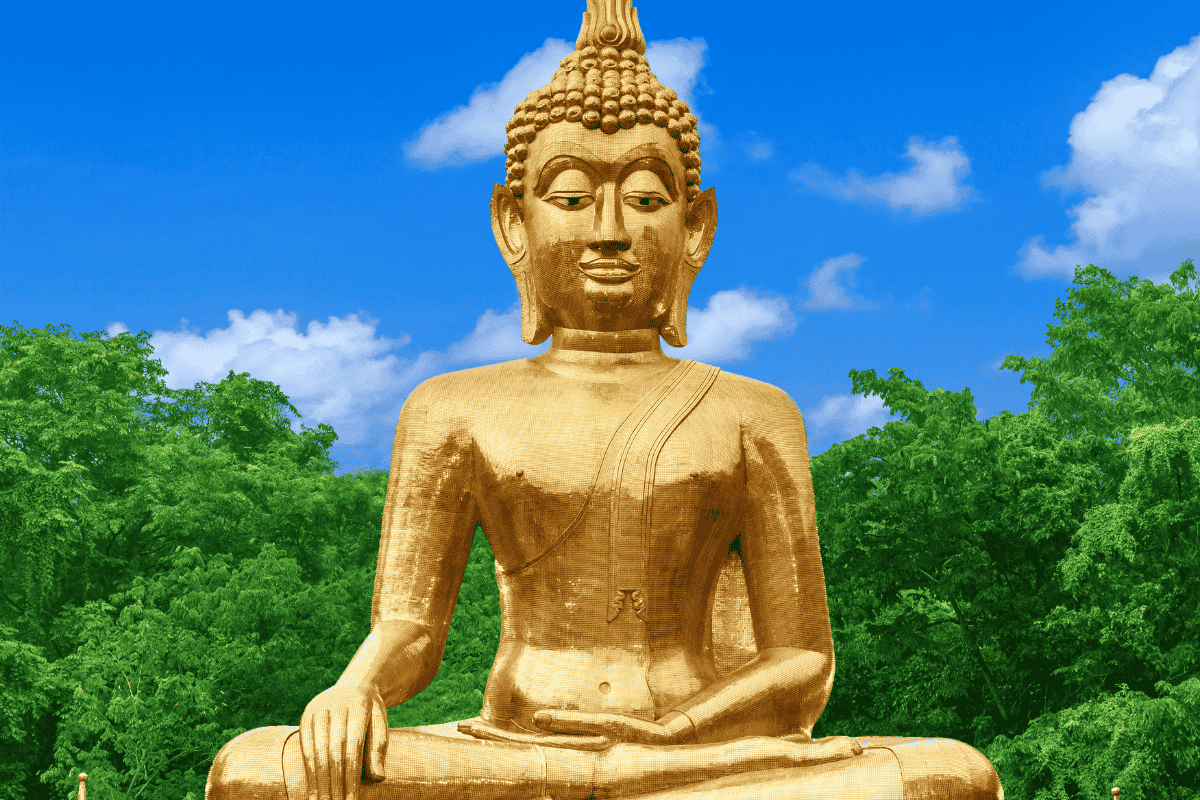 A large, serene golden Buddha statue in a meditative seated pose, set against a backdrop of lush green trees