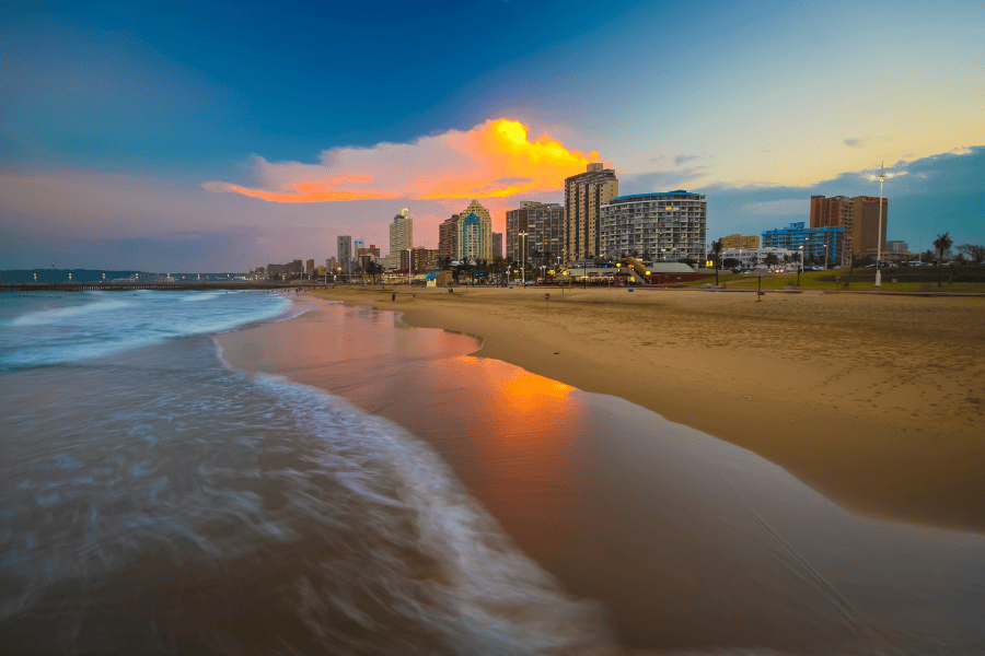 A wide-angle, long-exposure photo of a city skyline along a sandy beach at sunset.