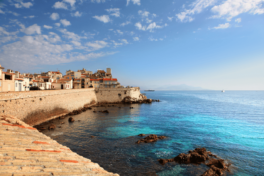 A scenic, wide-angle view of the historic coastal town of Antibes, France, situated along the sparkling turquoise waters of the Mediterranean Sea.